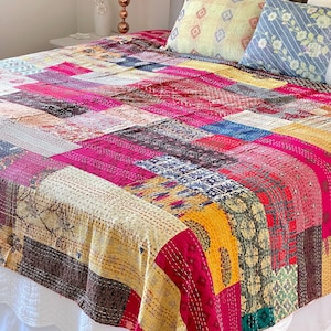 Op de afbeelding: Een kleurrijk patchwork-deken met verschillende stoffen en patronen in tinten roze, geel, blauw en bruin. Het deken is gemaakt met kantha-steken, een traditionele Indiase borduurtechniek.