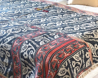 May include: A blue and red kantha quilt with a paisley pattern. The quilt is on a bed with white bedding and two gold throw pillows.