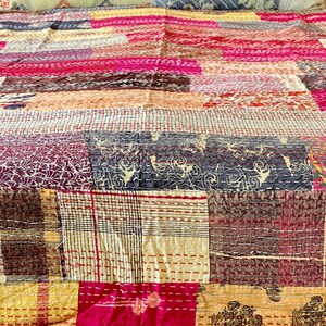 May include: A patchwork quilt featuring a mix of colours and patterns, including pink, brown, yellow, and white. The quilt is made from various fabrics stitched together in a random design.