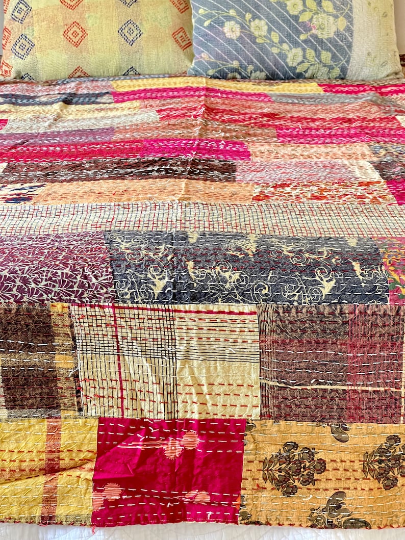 May include: A patchwork quilt featuring a mix of colours and patterns, including pink, brown, yellow, and white. The quilt is made from various fabrics stitched together in a random design.
