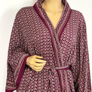 May include: A burgundy robe with a paisley pattern and a tie belt. The robe has a V-neck and long sleeves.