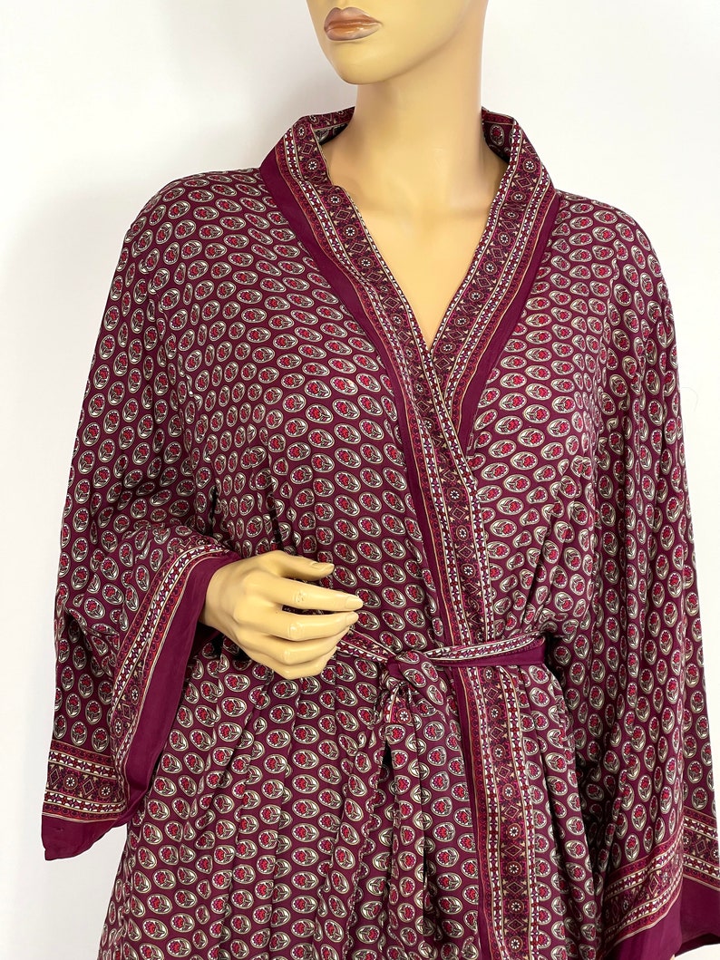May include: A burgundy robe with a paisley pattern and a tie belt. The robe has a V-neck and long sleeves.