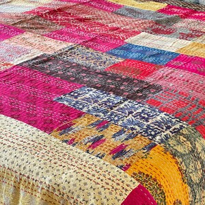 May include: A patchwork quilt featuring a mix of colours and patterns, including pink, yellow, blue, and brown. The quilt is made from various fabrics stitched together in a random design.