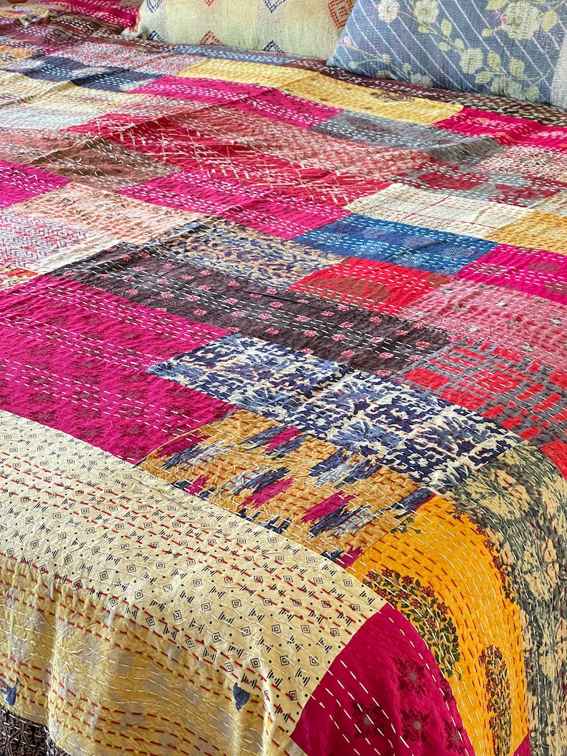May include: A patchwork quilt featuring a mix of colours and patterns, including pink, yellow, blue, and brown. The quilt is made from various fabrics stitched together in a random design.