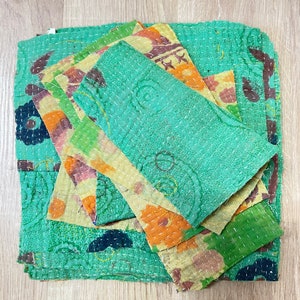 May include: A stack of colorful fabric squares with a green background. The fabric is quilted and has a floral pattern. The squares are layered on top of each other, creating a textured effect.