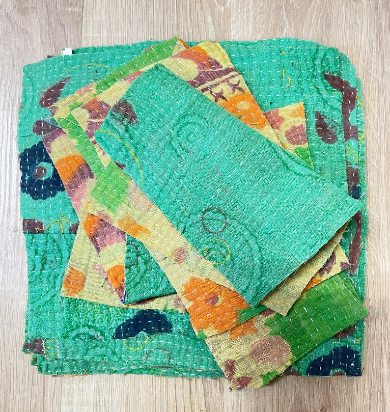May include: A stack of colorful fabric squares with a green background. The fabric is quilted and has a floral pattern. The squares are layered on top of each other, creating a textured effect.