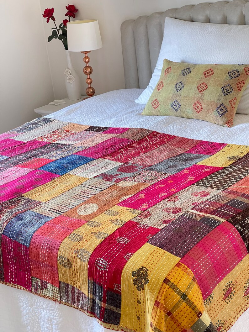 May include: A colourful patchwork quilt featuring a range of patterns and colours, including pink, yellow, blue, and brown. The quilt is made from kantha fabric and is ideal for adding a touch of bohemian style to any bedroom.