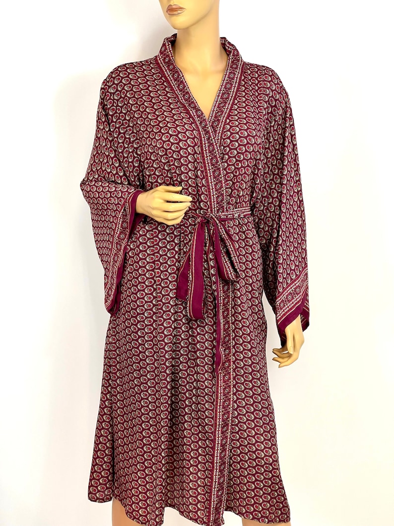 May include: A burgundy silk robe with a paisley pattern and a matching tie belt. The robe has long sleeves and a V-neck.