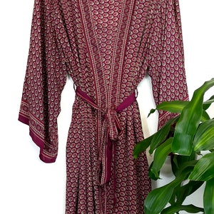 May include: A long, burgundy silk robe with a paisley print and a matching tie belt. The robe has a V-neck and long sleeves. The label on the robe reads "Tanga Nights".