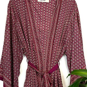May include: A burgundy silk robe with a paisley print and gold trim. The robe has a tie belt and long sleeves. The label on the robe reads "Tanya Leigh".