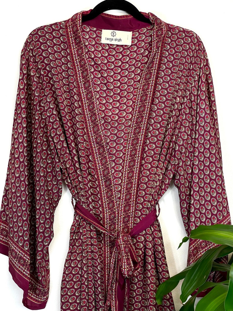 May include: A burgundy silk robe with a paisley print and gold trim. The robe has a tie belt and long sleeves. The label on the robe reads "Tanya Leigh".