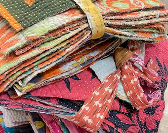 May include: A stack of colorful, stitched fabric squares, likely repurposed textiles. The fabrics display a variety of patterns and colors, including orange, green, red, and yellow. A coordinating fabric strip is wrapped around the stack.