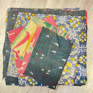 May include: A stack of colorful fabric squares with intricate patterns and stitching. The fabric is a mix of blue, green, yellow, red, and black.
