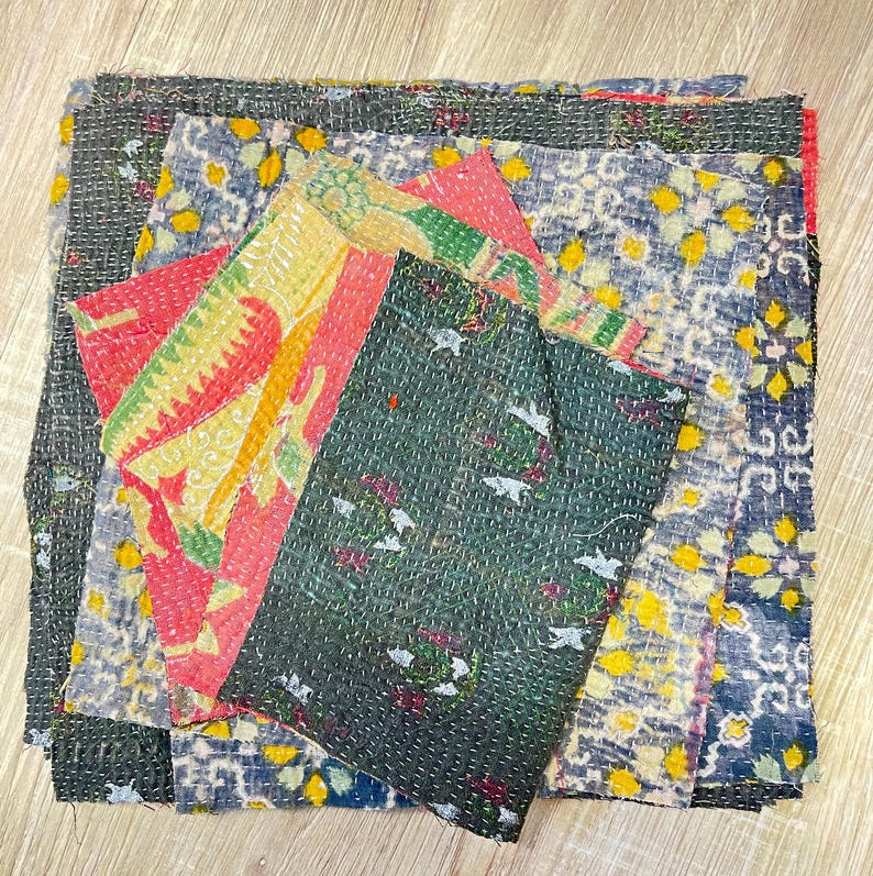 May include: A stack of colorful fabric squares with intricate patterns and stitching. The fabric is a mix of blue, green, yellow, red, and black.