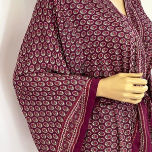 May include: A burgundy kimono with a floral pattern and a white trim. The kimono has a V-neck and a tie belt.