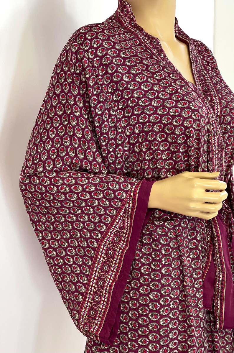 May include: A burgundy kimono with a floral pattern and a white trim. The kimono has a V-neck and a tie belt.