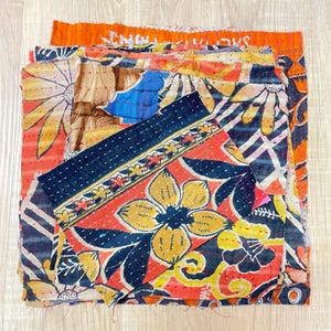 May include: A stack of colorful fabric scraps with floral patterns, some with black stitching. The fabric is a mix of red, orange, yellow, blue, and black.