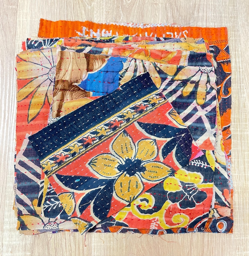 May include: A stack of colorful fabric scraps with floral patterns, some with black stitching. The fabric is a mix of red, orange, yellow, blue, and black.