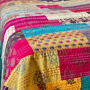 May include: A colourful patchwork quilt featuring a range of patterns and colours, including pink, yellow, blue, and brown. The quilt is made from various fabrics stitched together in a random design.