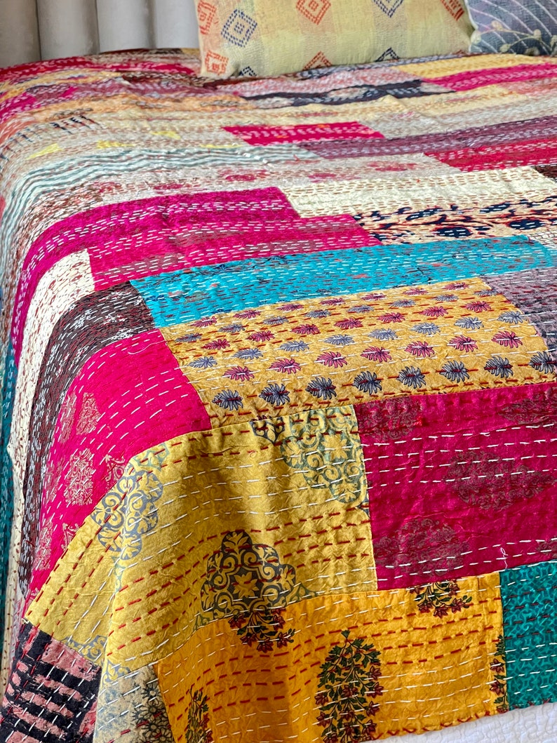 May include: A colourful patchwork quilt featuring a range of patterns and colours, including pink, yellow, blue, and brown. The quilt is made from various fabrics stitched together in a random design.