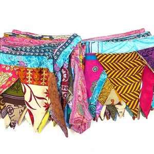 May include: A colorful fabric garland with a variety of patterns and colors, including pink, blue, yellow, and green. The garland is made of triangular pieces of fabric sewn together.