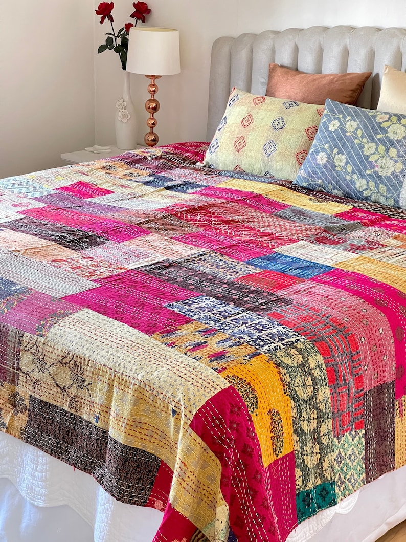 May include: A colourful patchwork quilt featuring a range of fabrics and patterns in shades of pink, yellow, blue, and brown. The quilt is crafted using kantha stitching, a traditional Indian embroidery technique.