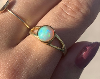 May include: A gold ring with a round opal gemstone. The opal has a rainbow of colors, including green, blue, and pink.
