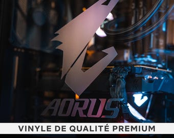 May include: Aorus logo vinyl decal in a silver color with a black background. The logo is a stylized eagle head with the word "AORUS" below it. The text "VINYLE DE QUALITÉ PREMIUM" is also visible in the image.