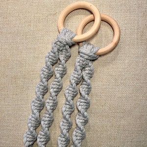May include: A gray macrame plant hanger with two wooden rings. The hanger is made of thick, twisted rope and is perfect for hanging a small plant.