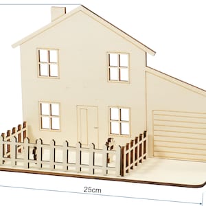 May include: A light-colored wooden house model featuring a front door, four windows, and an attached garage. A picket fence surrounds the front yard area. The structure measures 17.5 cm in height, 25 cm in width, and 12 cm in depth as indicated.