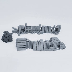 May include: A grey 3D printed model of a barricade made of wooden planks, barrels, and other debris. The barricade is broken and scattered, suggesting a scene of destruction.