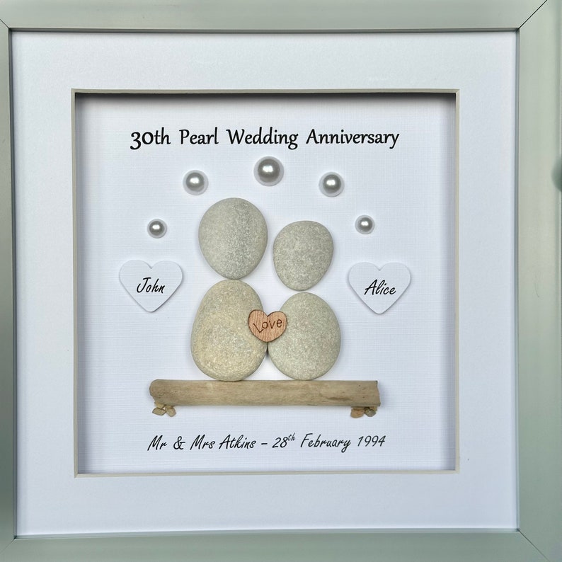 May include: A framed white background with two gray pebble figures representing a couple, with the words "John" and "Alice" on white hearts, and "Love" on a small brown heart. The text "30th Pearl Wedding Anniversary" and "Mr & Mrs Atkins - 28th February 1994" are also included.