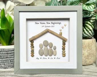 May include: A framed pebble art housewarming gift with the text "New Home, New Beginnings" and the date "29th September 2023". The house is made of driftwood and pebbles, and there are four pebble figures representing a family. The names "Amy", "Steven", "Livia", and "Jacob" are written below the house.