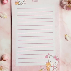 May include: Pink notepad with lined pages, featuring Hello Kitty and a teddy bear illustration. The notepad has the word "Notes" at the top. Cherry blossoms in pink and white surround the notepad, creating a soft, feminine aesthetic.