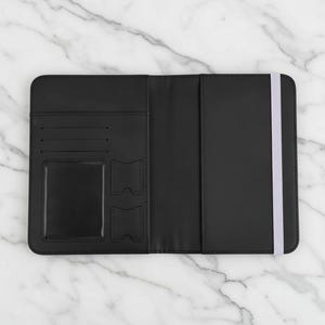 Puede incluir: Portapasaporte negro abierto con cierre de banda el&aacute;stica blanca. El interior presenta ranuras para tarjetas, una ventana de identificaci&oacute;n transparente y dos bolsillos adicionales. Sobre una superficie de m&aacute;rmol.