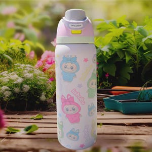 Puede incluir: Una botella de agua aislada blanca con una tapa rosa y verde claro. La botella est&aacute; decorada con personajes de dibujos animados de varios colores y la palabra "labubu". La tapa tiene el texto "Lift to Unlock".