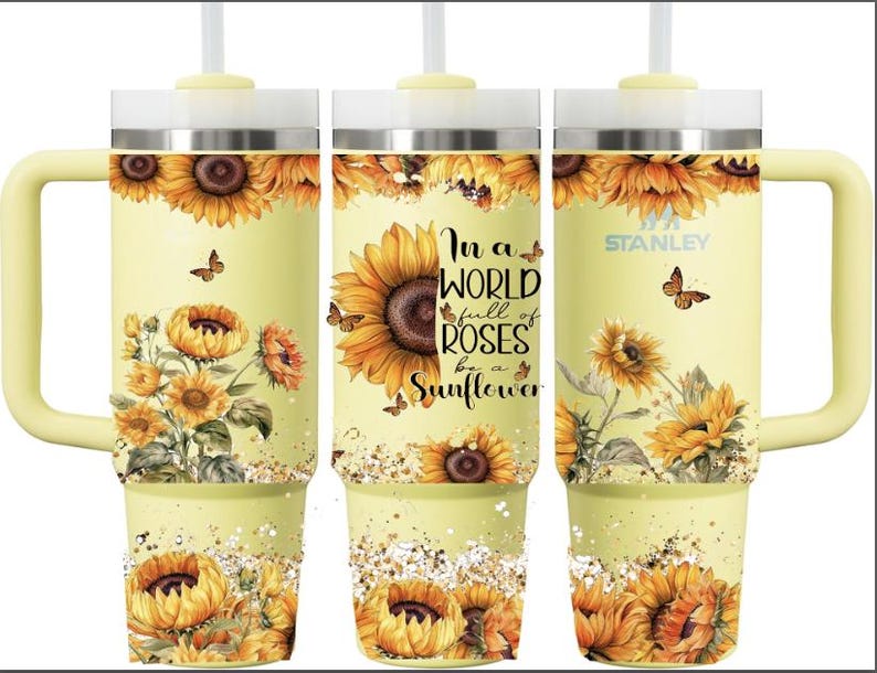 Puede incluir: Un vaso Stanley amarillo con un dise&ntilde;o de girasoles y mariposas, y el texto "In a world full of roses be a sunflower". El vaso tiene un asa y una pajita.