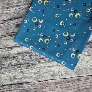 Könnte beinhalten: Tealfarbener Stoff mit einem sich wiederholenden Muster aus gelben, schwarzen und rosa Kreisen. Der Stoff hat eine glatte Textur.