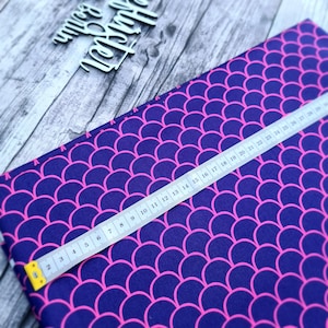 Könnte beinhalten: Nahaufnahme eines dunkelblauen Stoffes mit einem rosafarbenen Schuppenmuster. Ein Maßband liegt über dem Stoff und zeigt die Maße in Zentimetern.