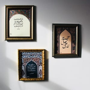 May include: Three framed artworks with gold and black frames are displayed on a white wall. The art showcases calligraphy and decorative patterns in red, blue, and gold. The rectangular frames have intricate detailing, enhancing the aesthetic appeal of the wall decor.