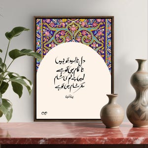 Puede incluir: Obra de arte enmarcada con patrones florales en azul, rosa y amarillo. La obra tiene un panel central crema con caligrafía negra. Jarrones decorativos y una planta en primer plano.