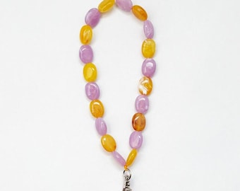May include: A phone charm made of purple and yellow oval beads with a silver clasp. The charm is attached to a pink phone case.