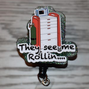 K&ouml;nnte beinhalten: Ein glitzerndes Ausweis-Jojo mit einem medizinischen Wagen, einer Sauerstoffflasche und dem Text "They see me Rollin...". Der Wagen ist rot und wei&szlig;, mit einem kleinen Monitor. Das Jojo ist schwarz.