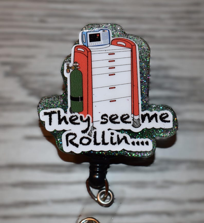 K&ouml;nnte beinhalten: Ein glitzerndes Ausweis-Jojo mit einem medizinischen Wagen, einer Sauerstoffflasche und dem Text "They see me Rollin...". Der Wagen ist rot und wei&szlig;, mit einem kleinen Monitor. Das Jojo ist schwarz.