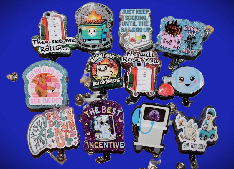 K&ouml;nnte beinhalten: Eine Sammlung glitzernder Ausweisrollen mit verschiedenen Designs und Texten. Die Designs umfassen einen M&uuml;llcontainer mit Flammen, einen Toaster, einen B&auml;ren, der einen Topf umr&uuml;hrt, und medizinische Ger&auml;te. Texte sind "They see me Rollin...", "Burnt Out" und "The Best Incentive."