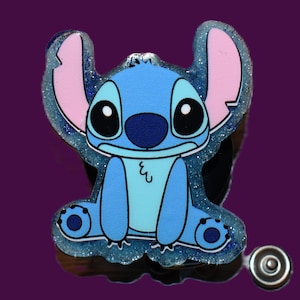 May include: A blue and light blue cartoon character with large black eyes and pink ears. The character is surrounded by a glittery, light blue border. The image is set against a dark purple background.