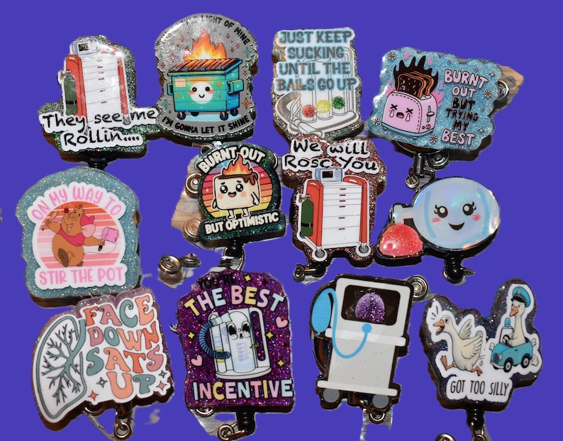 K&ouml;nnte beinhalten: Eine Sammlung von glitzernden Ausweisrollen im Cartoon-Stil mit verschiedenen Designs und Phrasen. Die Designs umfassen einen brennenden M&uuml;llcontainer, einen Toaster und medizinische Ger&auml;te. Texte sind "They see me rollin", "Burnt out but optimistic" und "The best incentive".