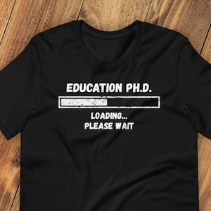 May include: Black t-shirt with white text that reads "EDUCATION PH.D. LOADING... PLEASE WAIT". The text is in a progress bar format.