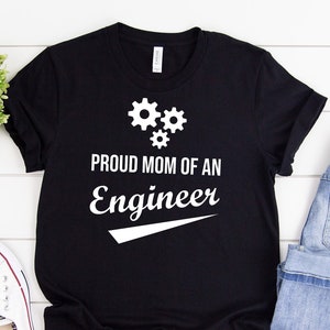 May include: Black t-shirt with white text that reads "Proud Mom of an Engineer" with a white gear design above the text.