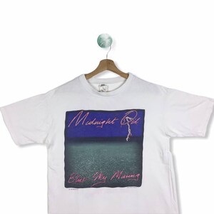 May include: White t-shirt with a graphic print of the album cover for "Midnight Oil - Blue Sky Mining".